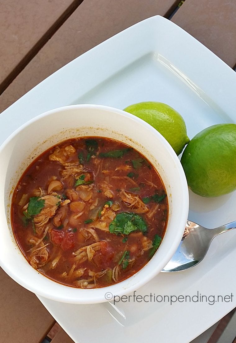 Crockpot chalupa soup in white bowl on white plate with two limes in background