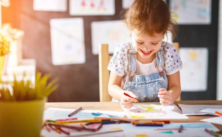 child girl draws with colored pencils in kindergarten