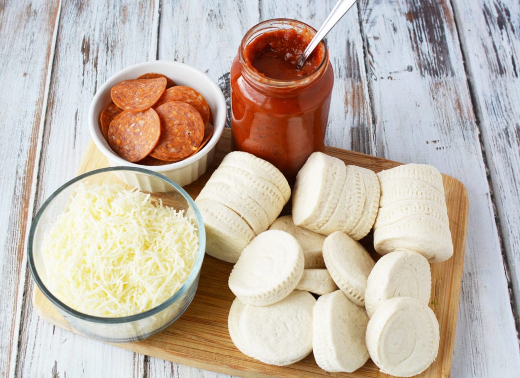 ingredients on cutting board including pepperoni, pizza sauce, cheese, and canned biscuits