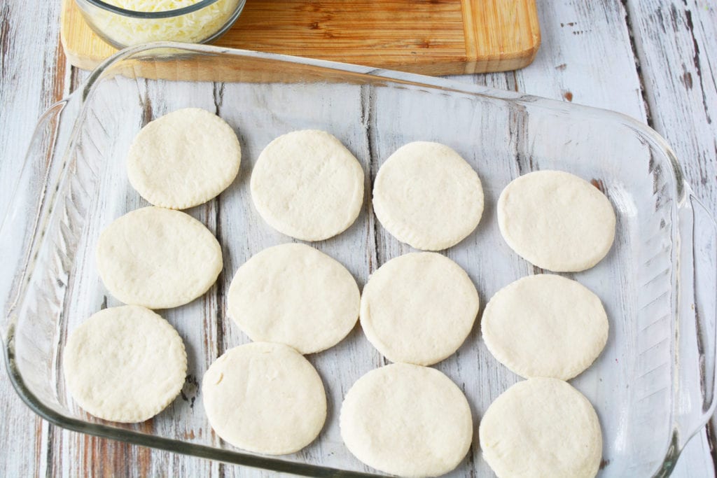 glass pan with 12 biscuits layered on bottom for pizza bake 