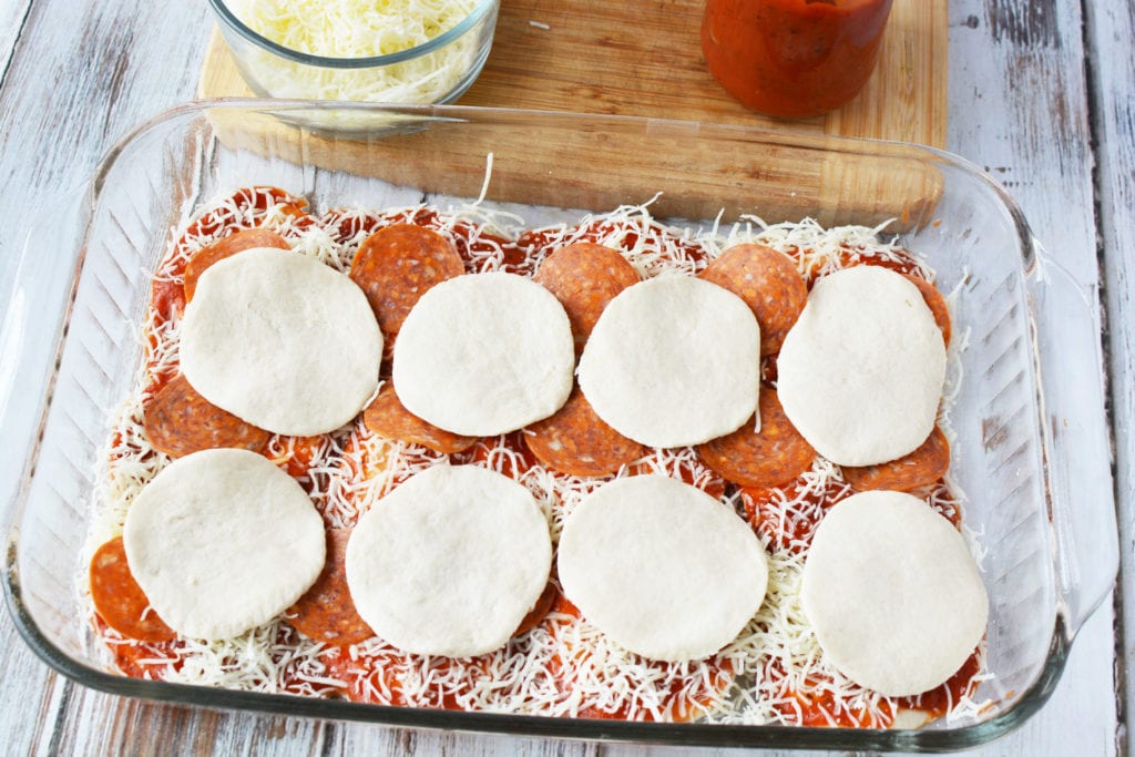 glass pan with biscuits on top of first pizza bake layer