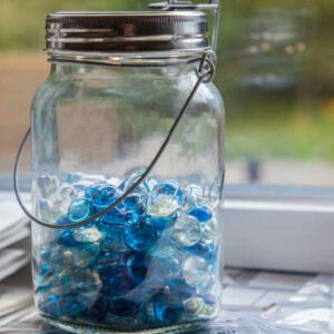 jar with blue marbles sitting in front of window marble jar