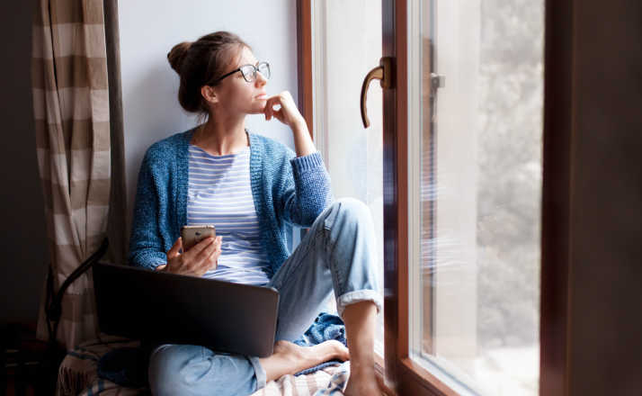 mom sitting on windowsill looking out window with phone and laptop how to get a break from your kids