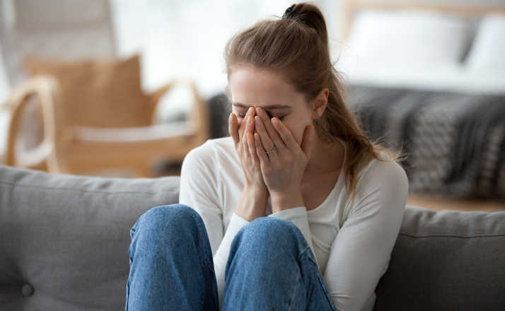 mom with ponytail sitting on the couch with her head in her hands and knees up emetophobia