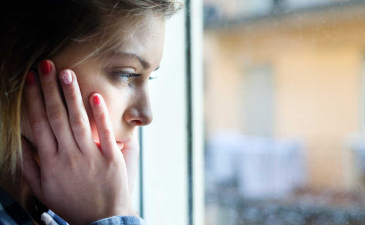 Sad face expression of young woman next to window