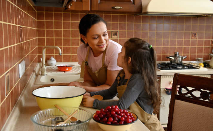 Mom and daughter in kitchen with bowl of cherries looking at each other