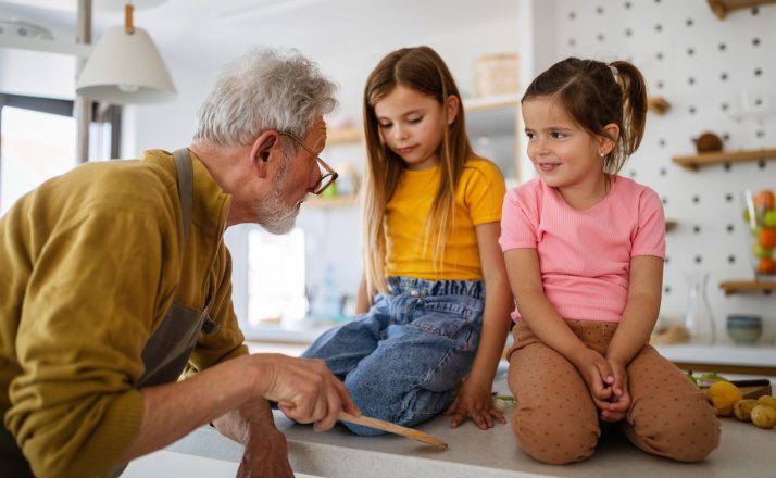 How to deal with narcissistic grandparents. Grandpa with two granddaughters sitting on kitchen counter getting scolded